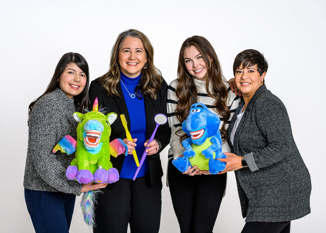 Picture of 4 dental team members standing and smiling, one holding a unicorn puppet and one holding a dinosaur puppet. Dentist holding a large toothbrush and mouth mirror.